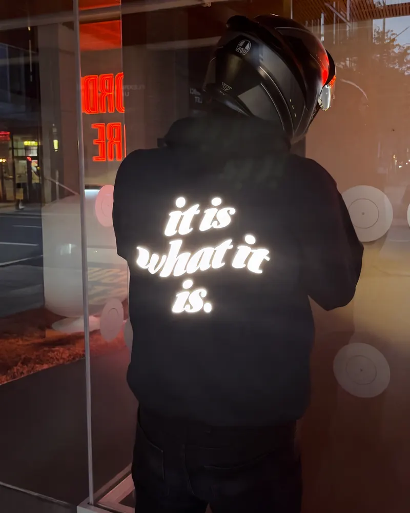 IT IS WHAT IT IS hoodie print lit up white under street light